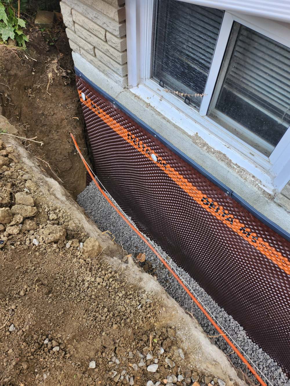 Exterior foundation wall with dimple membrane, new weeping tile and clear stone in an open trench