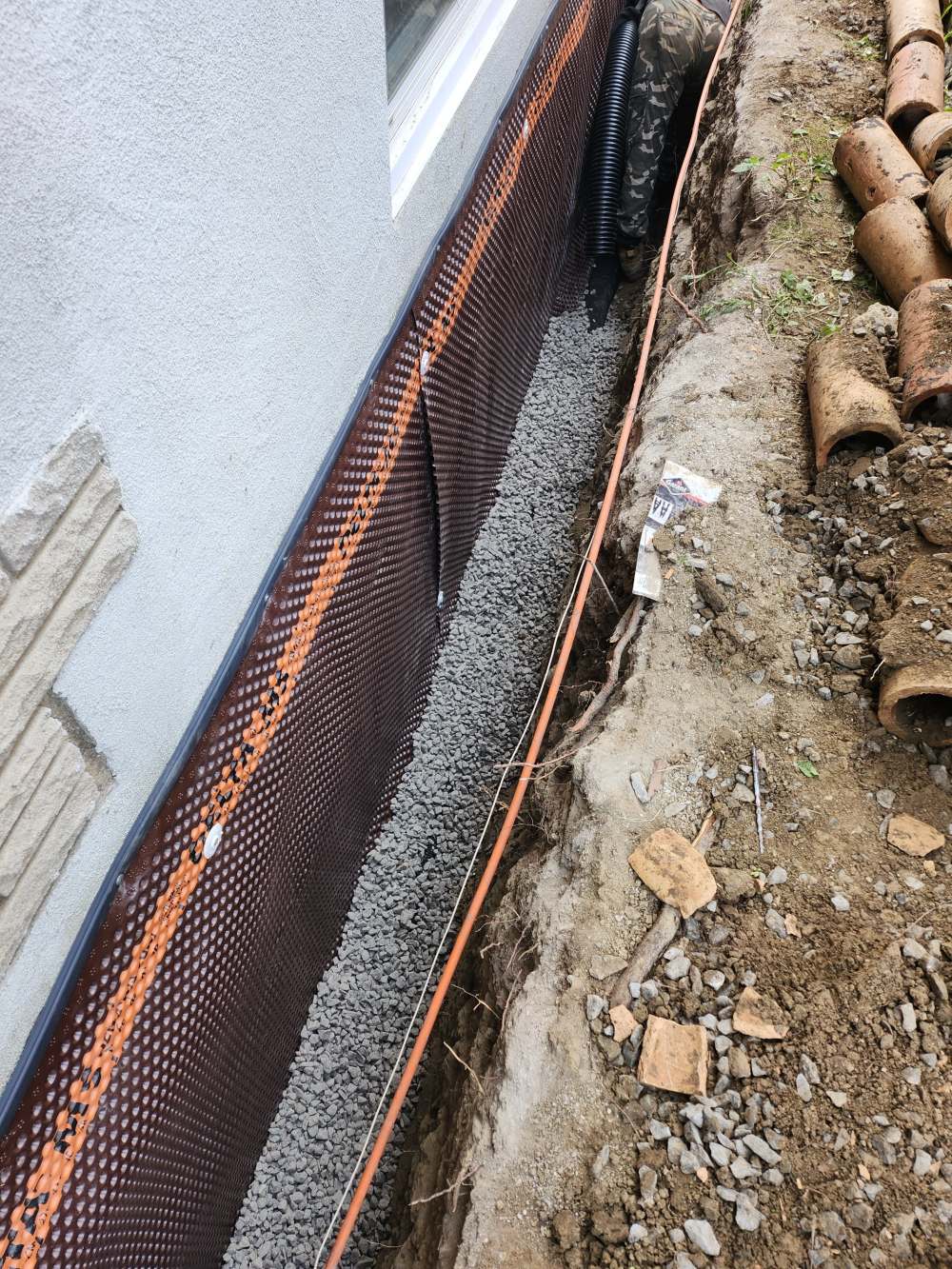 Open trench with membrane, clear stone and new weeping tile along a foundation