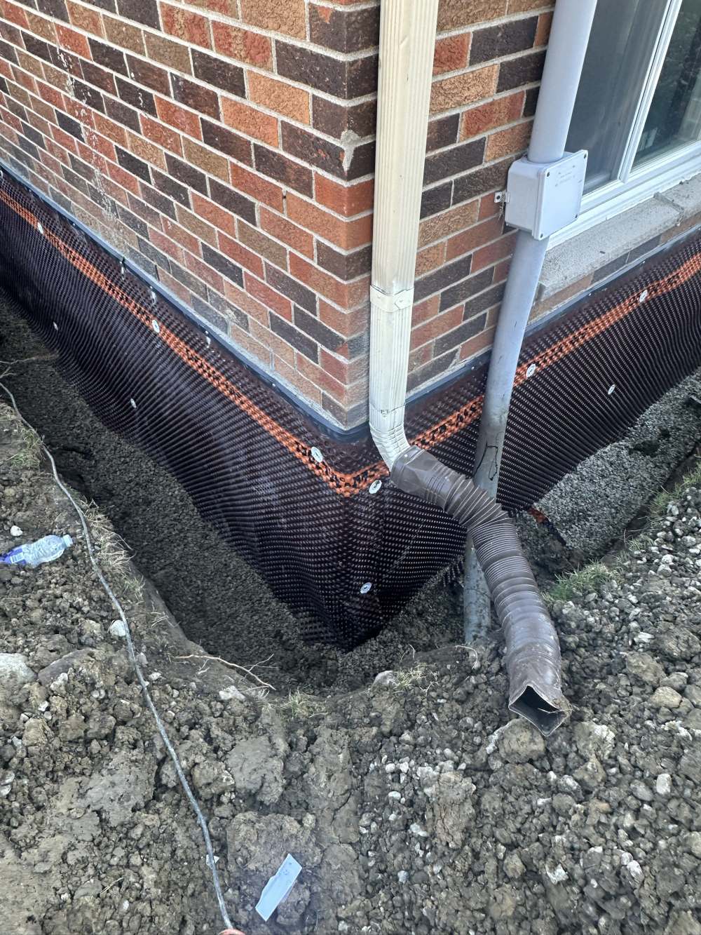 Finished foundation corner with membrane and the downspout tied into the drainage